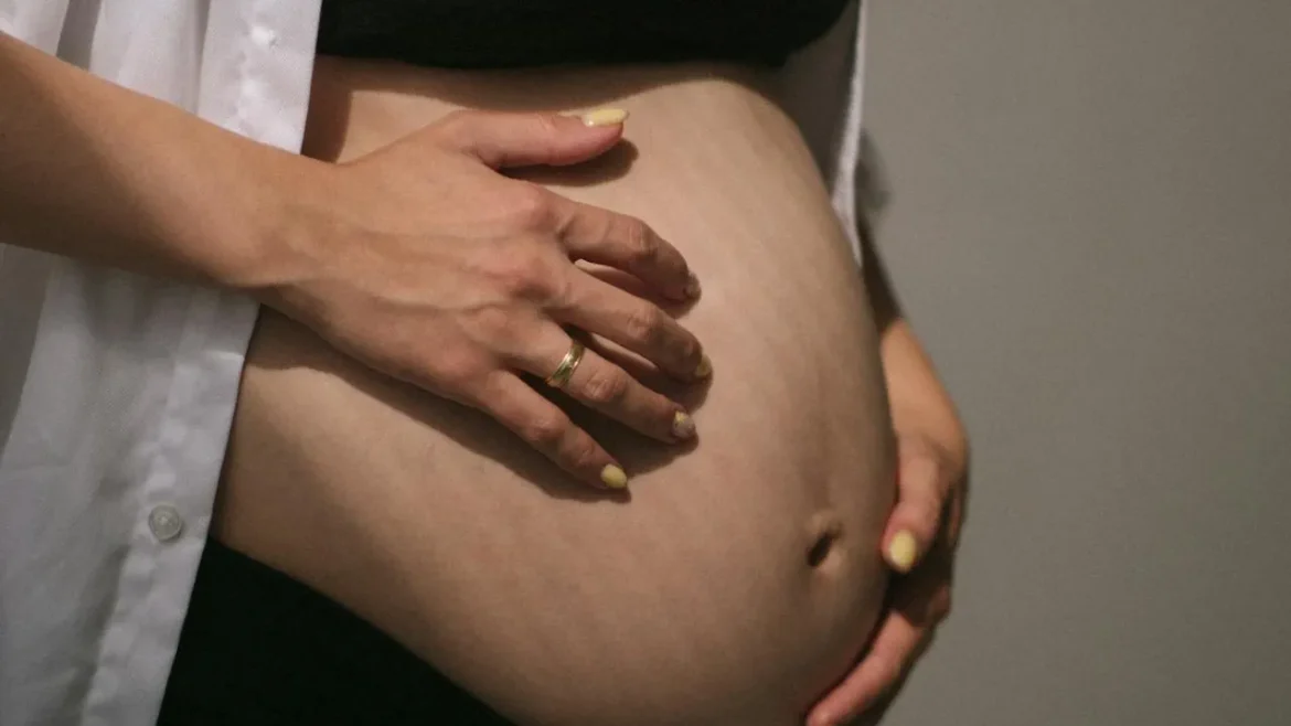 Zbliżenie na brzuch kobiety po ciąży, delikatnie obejmowany dłońmi.