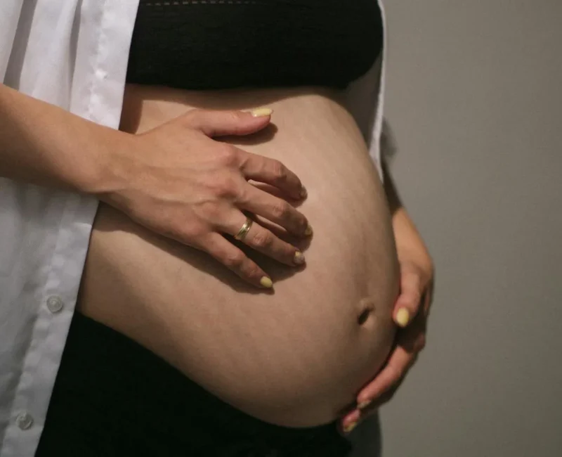 Zbliżenie na brzuch kobiety po ciąży, delikatnie obejmowany dłońmi.