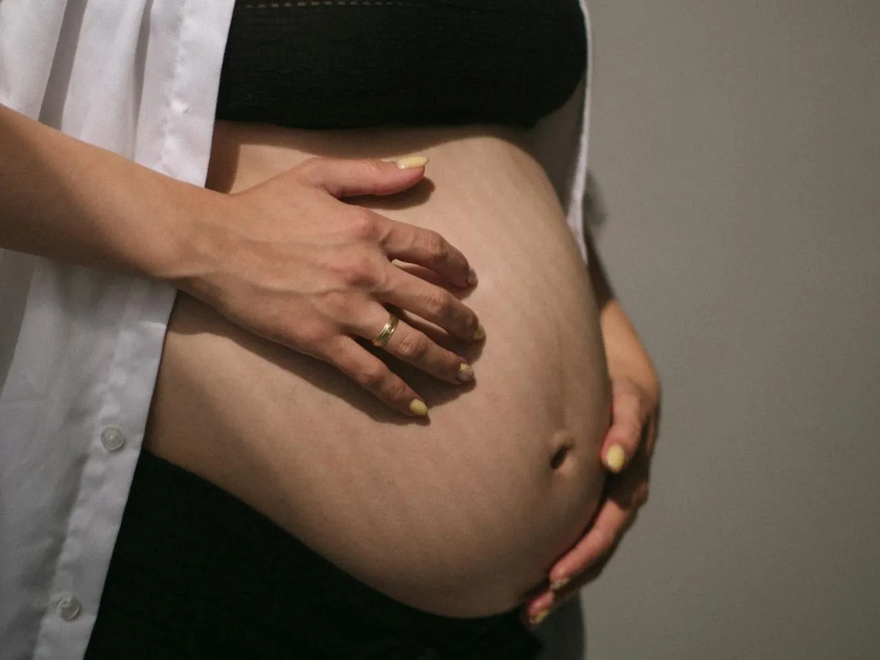 Zbliżenie na brzuch kobiety po ciąży, delikatnie obejmowany dłońmi.