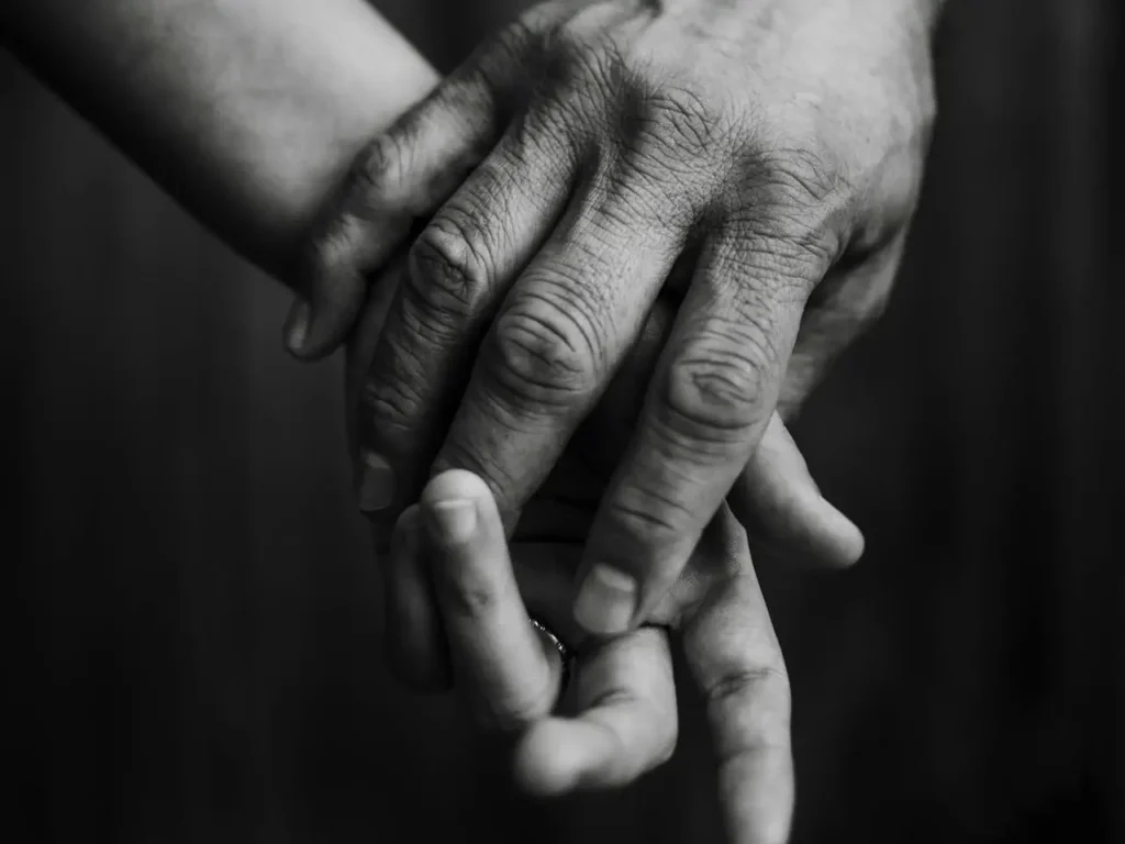 Dłoń dorosłej osoby obejmuje mniejszą dłoń dziecka lub partnera, czarno-białe zdjęcie