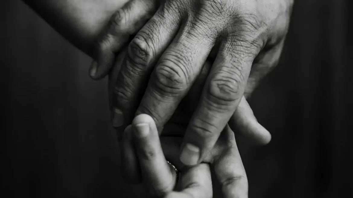 Dłoń dorosłej osoby obejmuje mniejszą dłoń dziecka lub partnera, czarno-białe zdjęcie