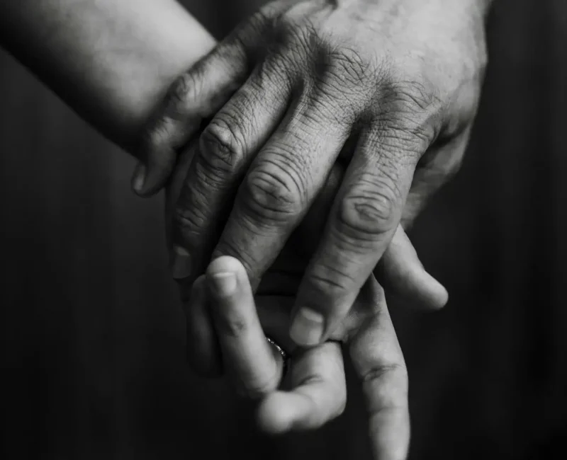 Dłoń dorosłej osoby obejmuje mniejszą dłoń dziecka lub partnera, czarno-białe zdjęcie