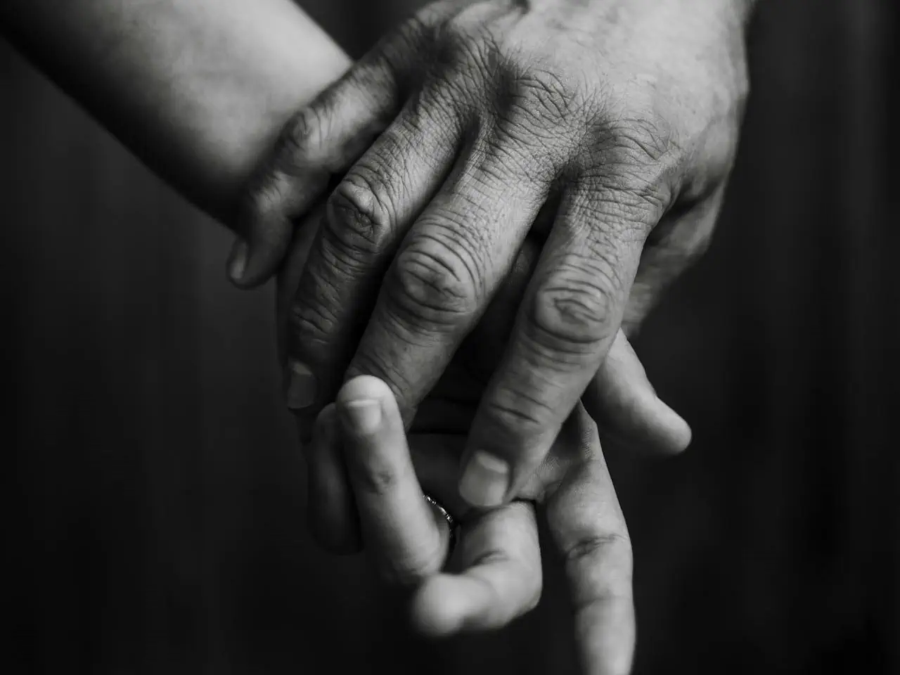 Dłoń dorosłej osoby obejmuje mniejszą dłoń dziecka lub partnera, czarno-białe zdjęcie