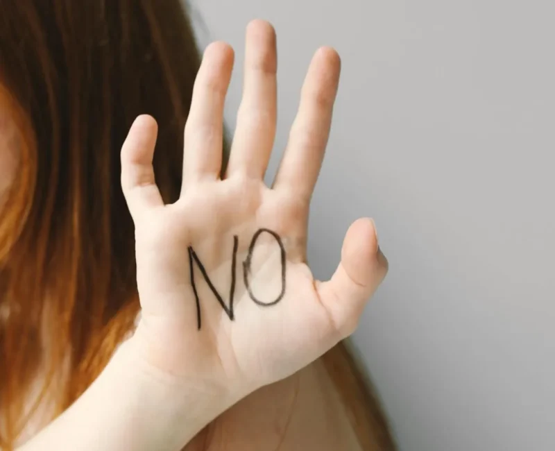 Uniesiona dłoń z napisem „NO” na wewnętrznej stronie, symbolizująca stawianie granic, asertywność i odmowę.
