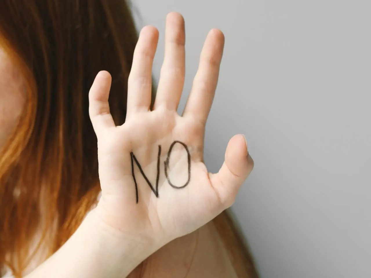 Uniesiona dłoń z napisem „NO” na wewnętrznej stronie, symbolizująca stawianie granic, asertywność i odmowę.