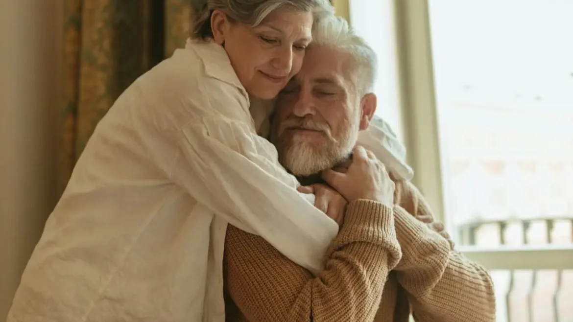 Dojrzała para przytula się czule w domowym wnętrzu, wyrażając bliskość, czułość i intymność w późniejszym wieku.